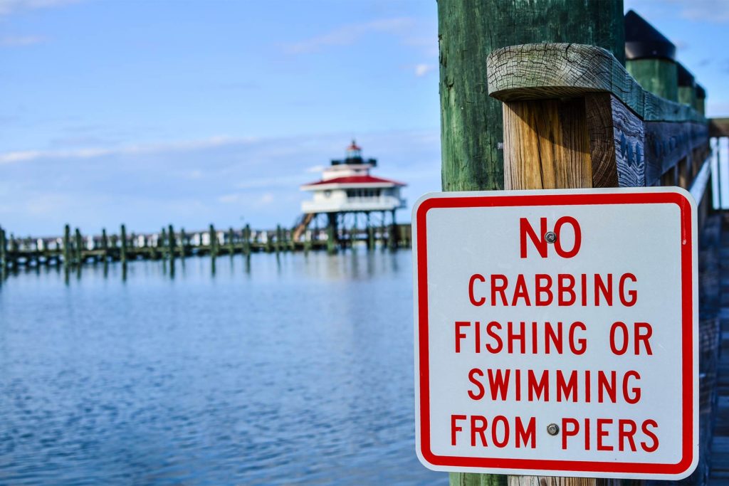 A sign saying "No crabbing fishing or swimming from piers" next to a pier in the Chesapeake Bay