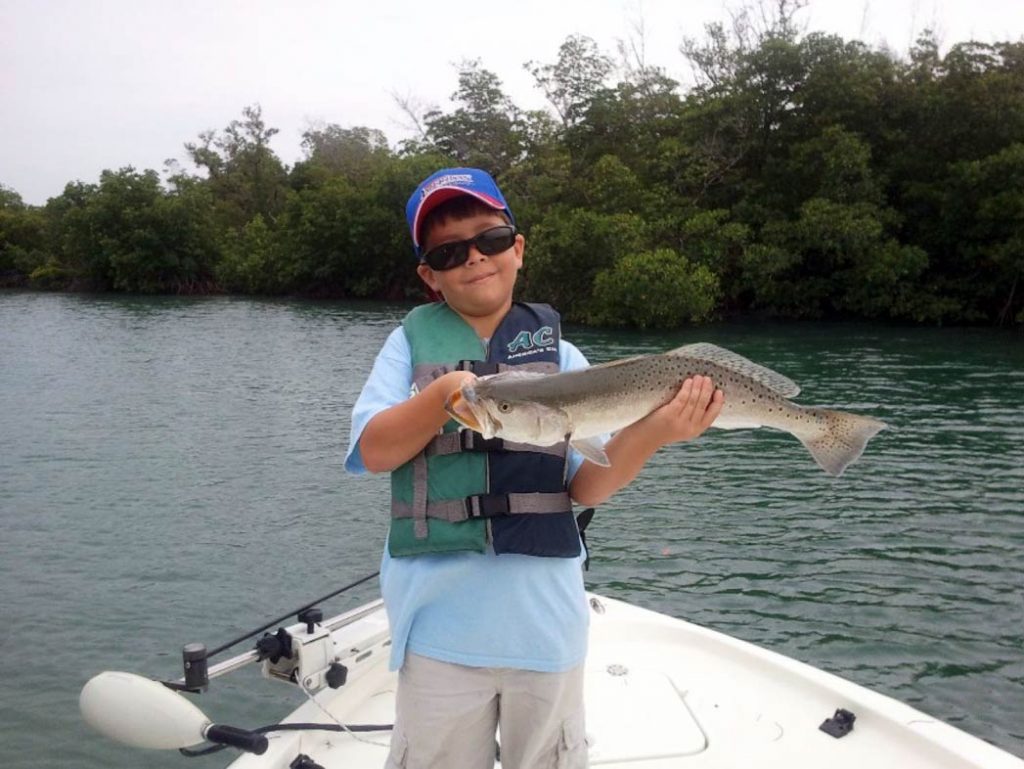 A boy proudly displays his Speckled Trout on board a boat on the Indian River