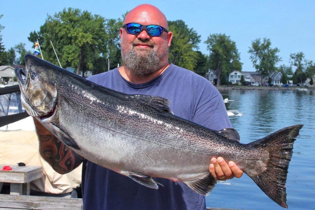 Ein männlicher Angler, der einen großen Chinook Lachs hält.