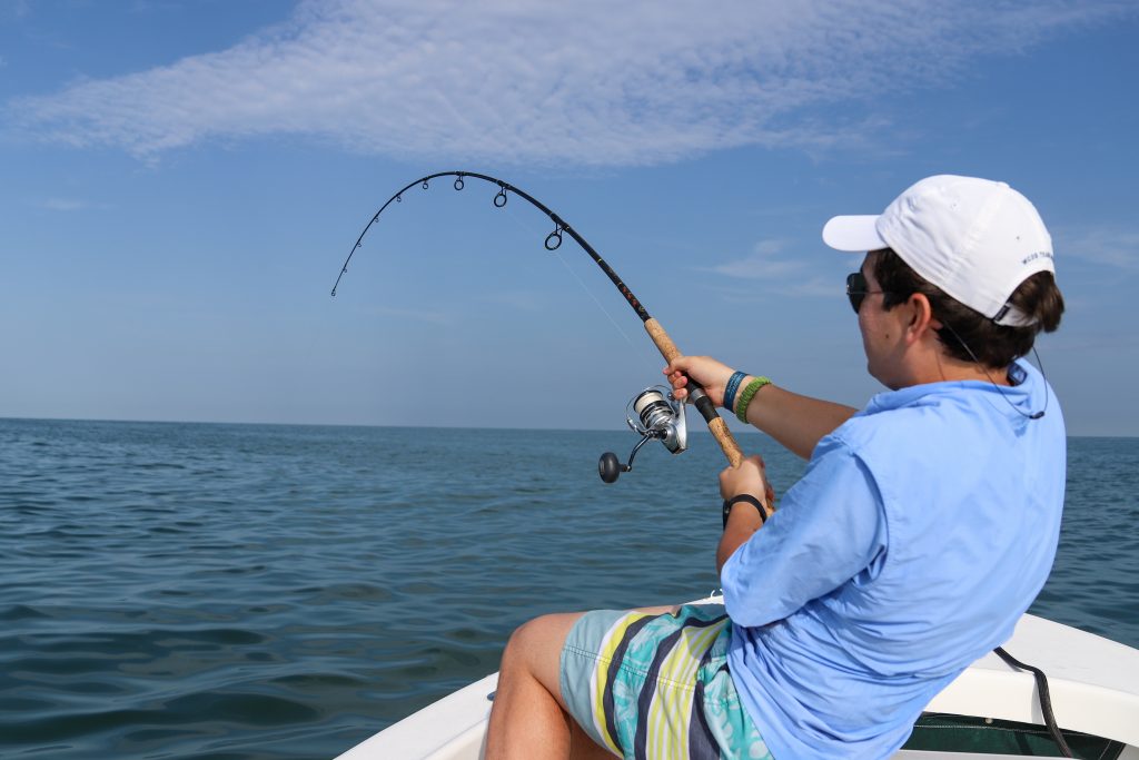 A man holding fishing on a boat. He is holding a rod which is bent from the strain of reeling in a big fish.