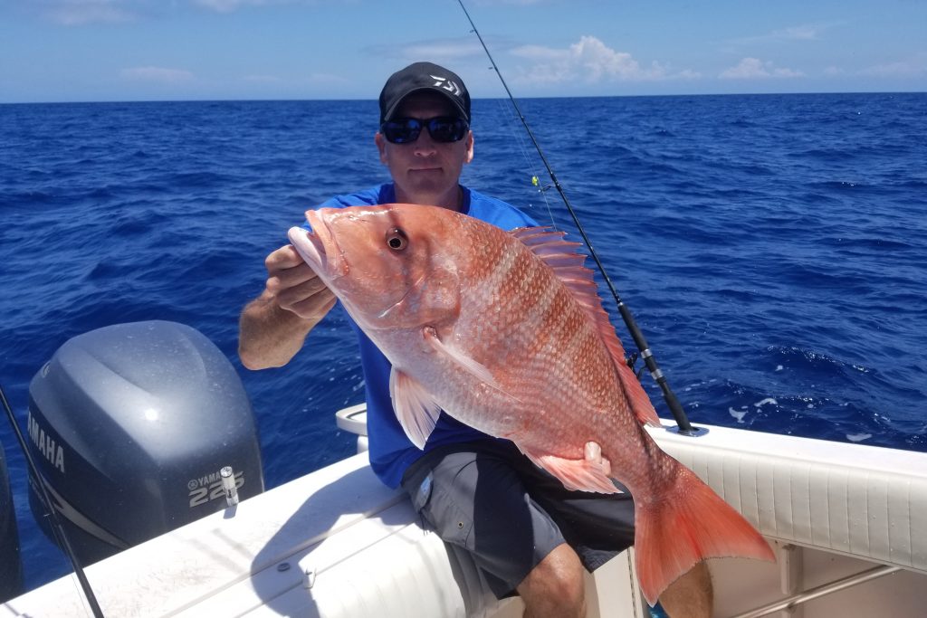 A man holding up a Red Snapper on a charter fishing boat