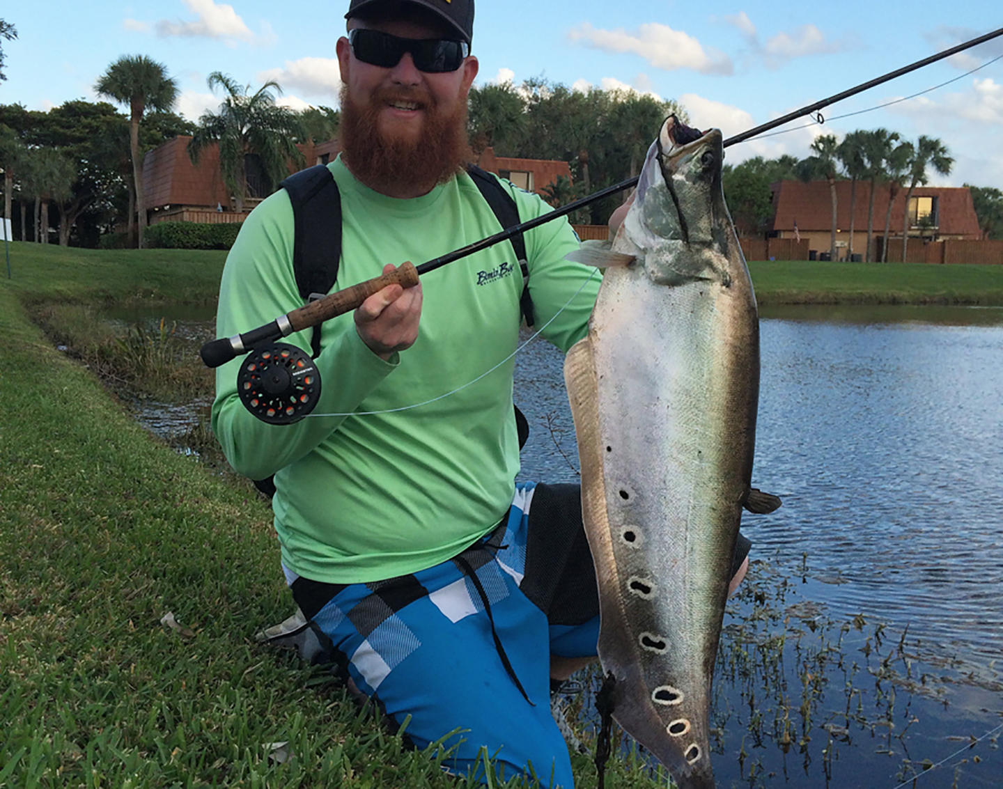 An anglers holding a fly fishing rod and an invasive clown knife fish.