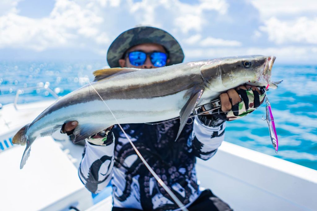 Een visser houdt een Cobia omhoog aan boord van een charterboot. 