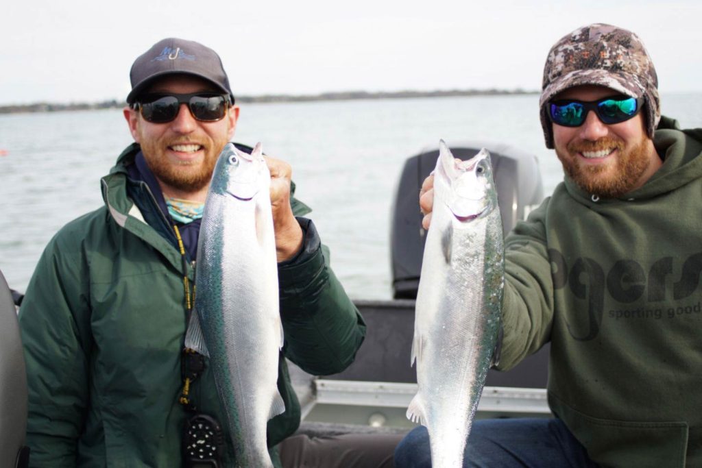 Two men hold two Coho Salmon on a charter boat with Lake Michigan behind them