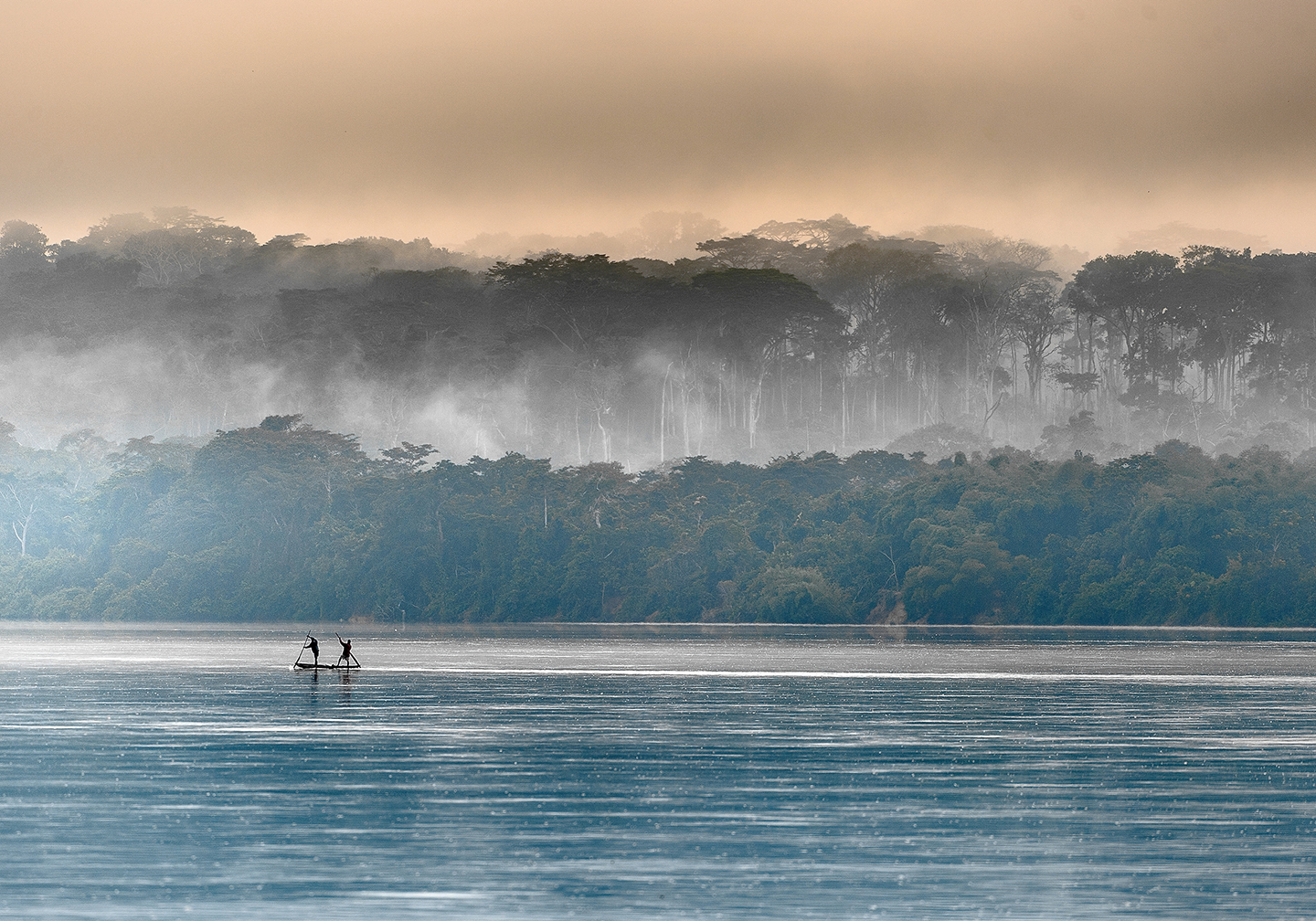 Two fishermen in the distance on the Congo River, with trees and sky behind them