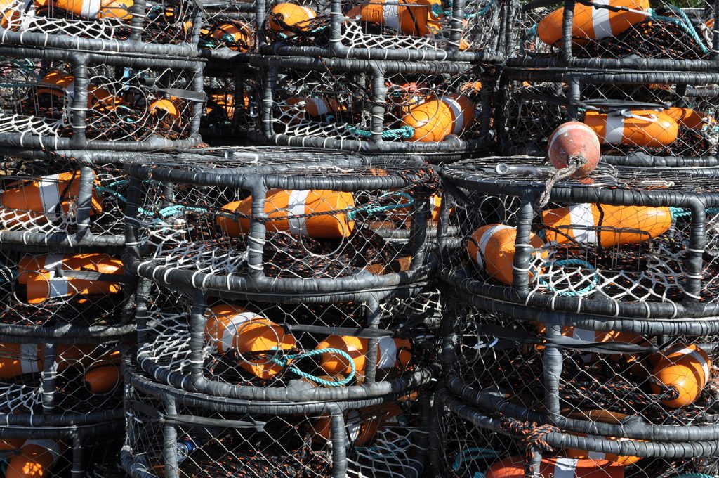 A stack of black commercial crab pots with orange floats.