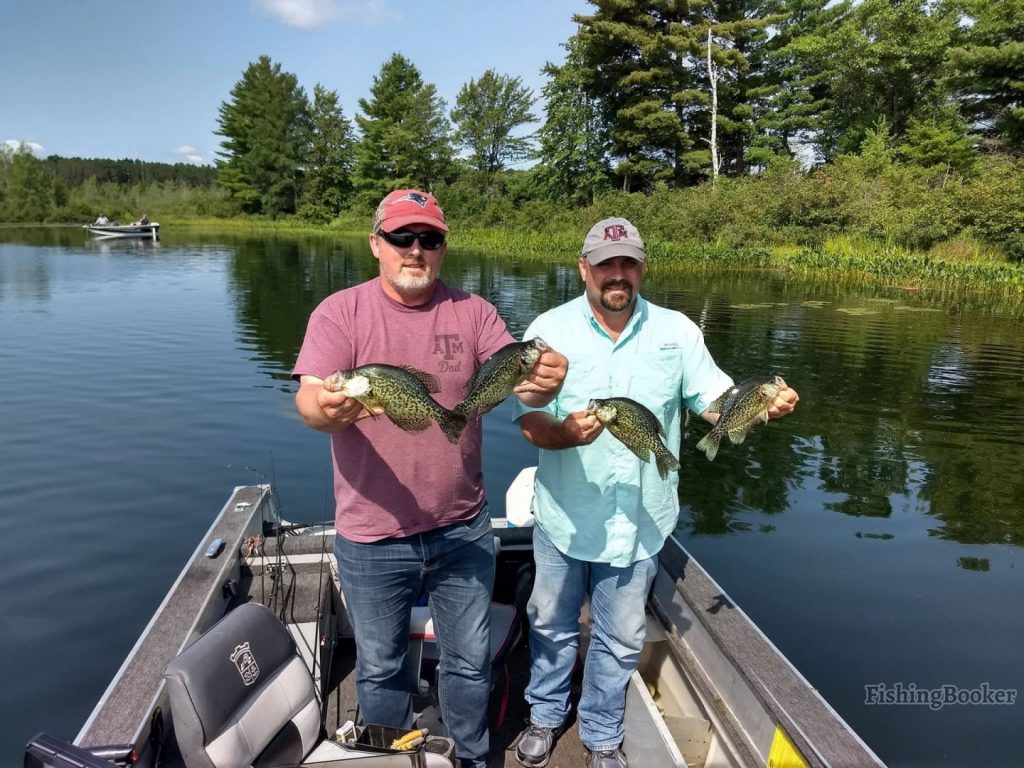 Two fishermen standing on a boat holding four Crappie fish