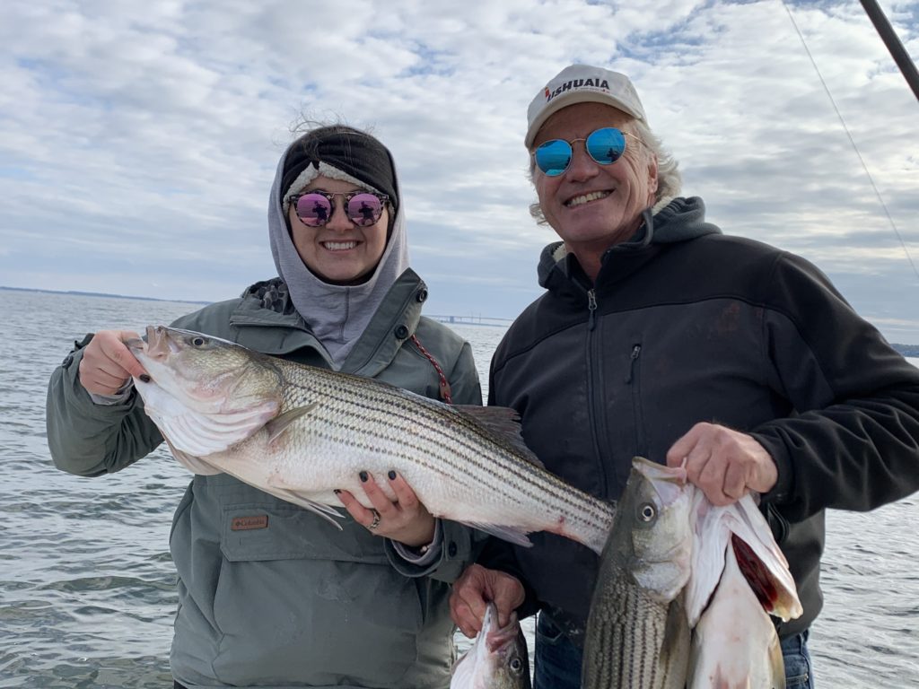 Father and daughter holding Rockfish they caught on a fishing charter, showing that fishing is a great guilt-free activity for family reunions during the pandemic