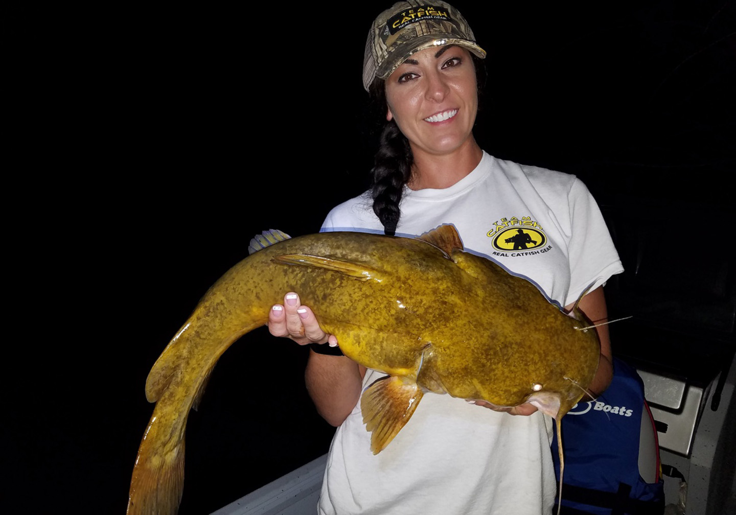 A smiling lady holding a Flathead Catfish at night