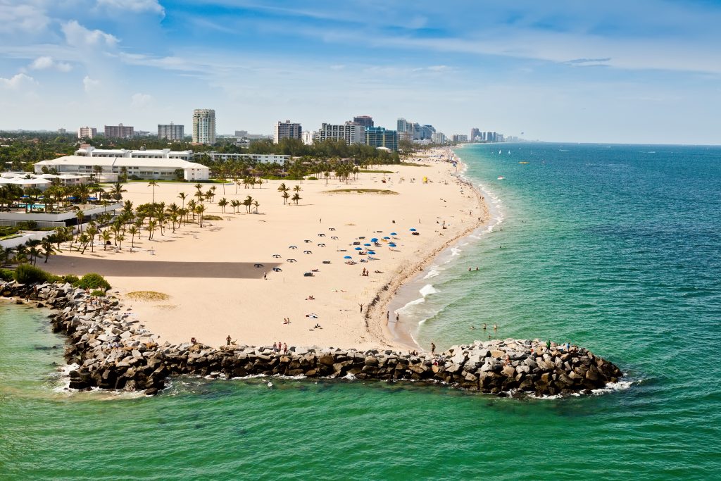 An aerial view of Fort Lauderdale Beach from the inlet, with people fishing on the jetty in the foreground