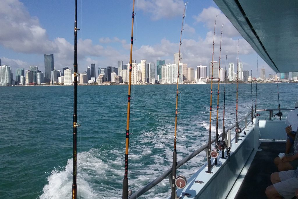 Una vista a lo largo de la cubierta de un barco de pesca de fiesta, con cañas alineadas y el horizonte de Fort Lauderdale al fondo