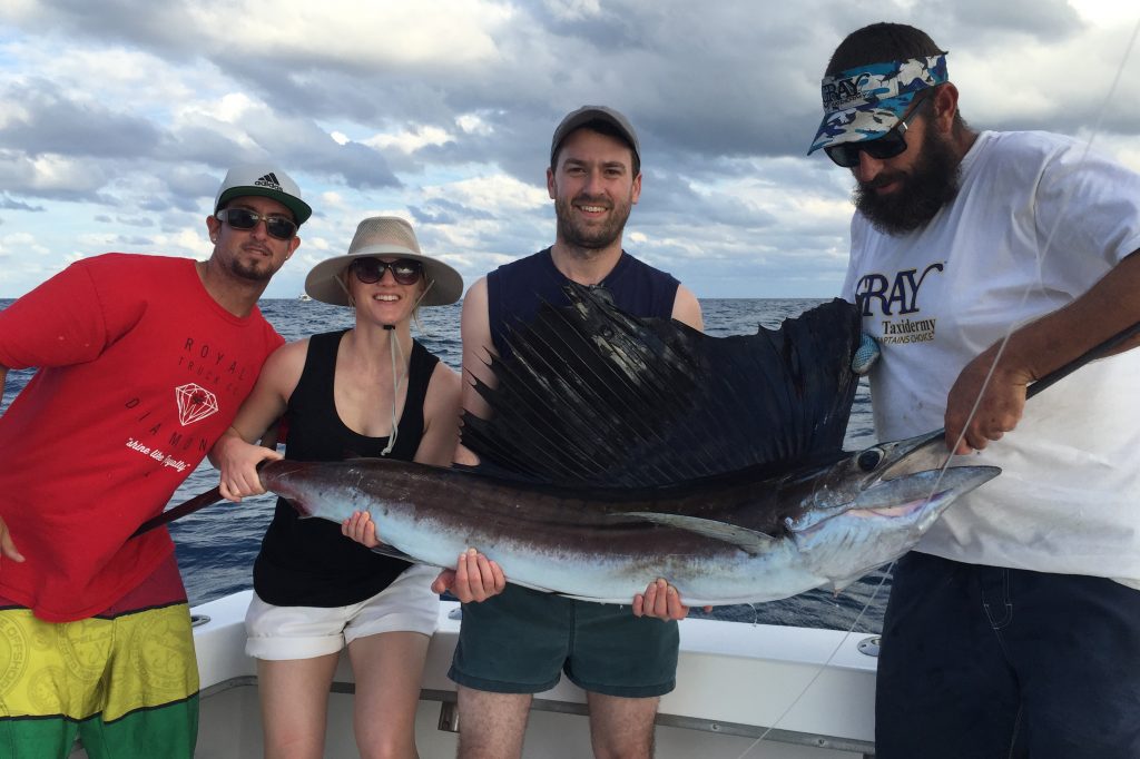 Four people holding a large Sailfish, while standing on a fishing boat