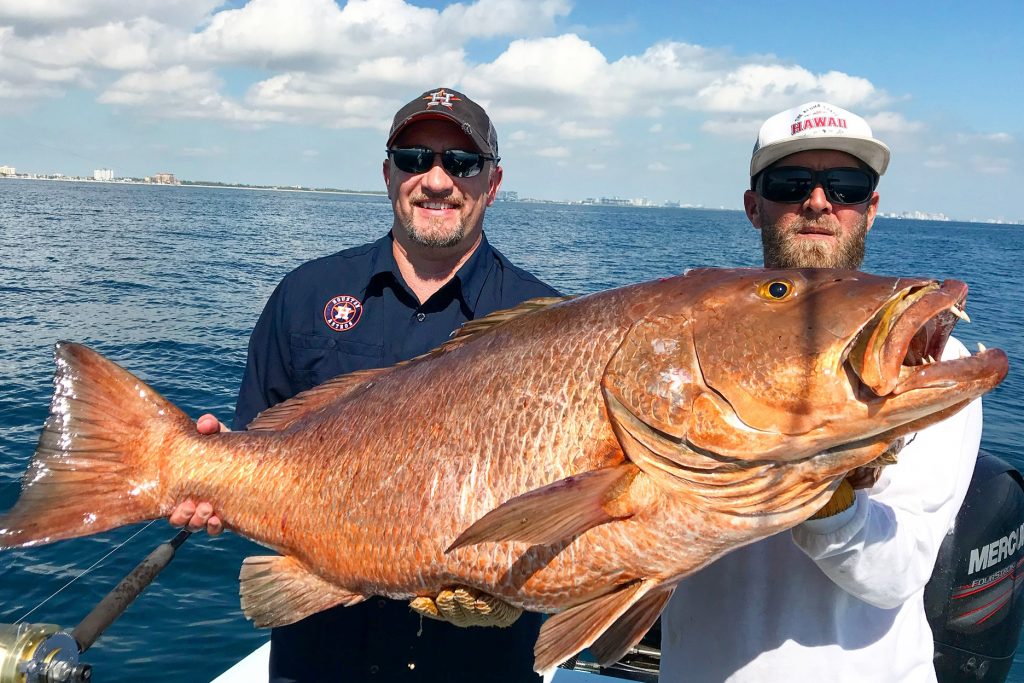 Two men holding a giant Cubera Snapper caught while fishing in Fort Lauderdale