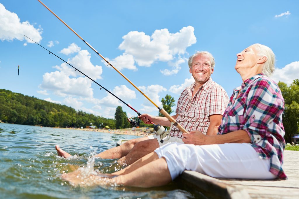 An elderly couple laughing and fishing with their feet in the water