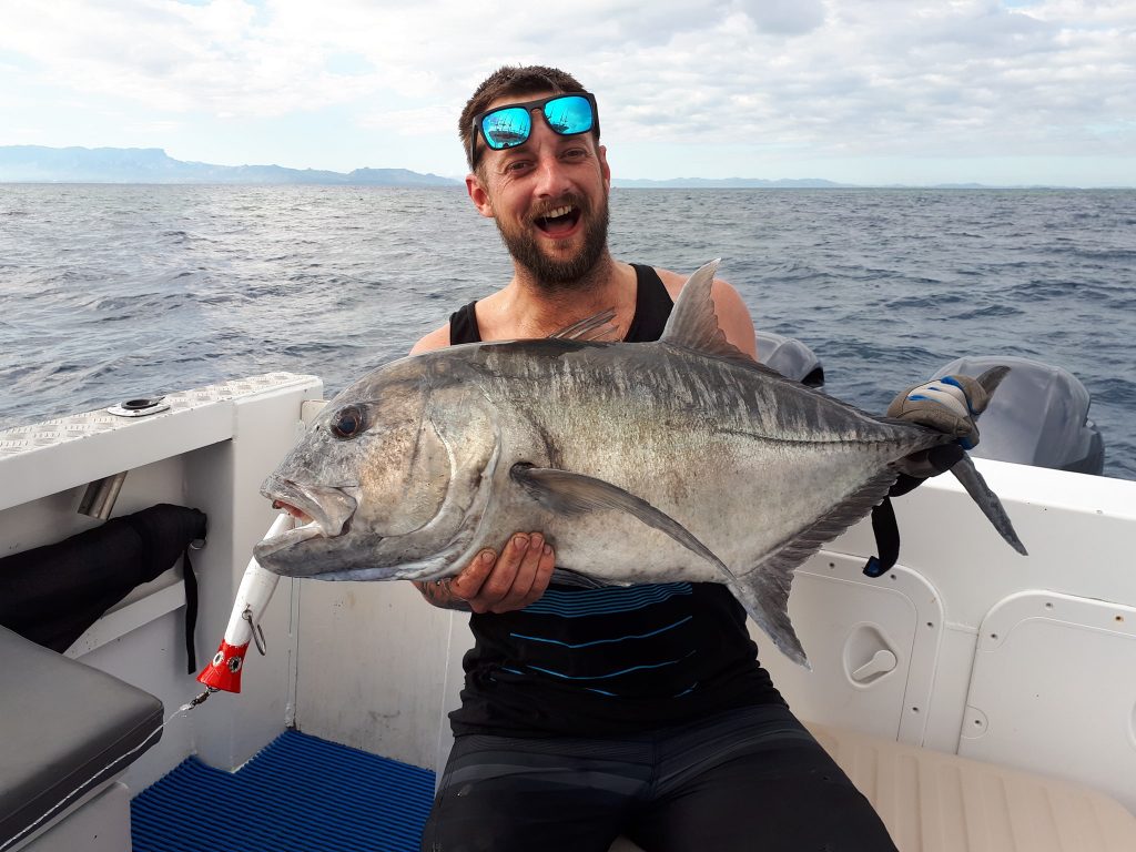 a smiling angler posing with a Giant Trevally caught on a lure