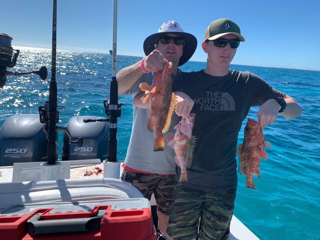 Two young anglers standing on a boat holding three small Grouper