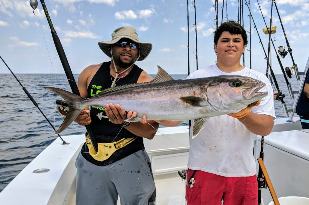 Two anglers holding a large Amberjack on a sportfishing boat