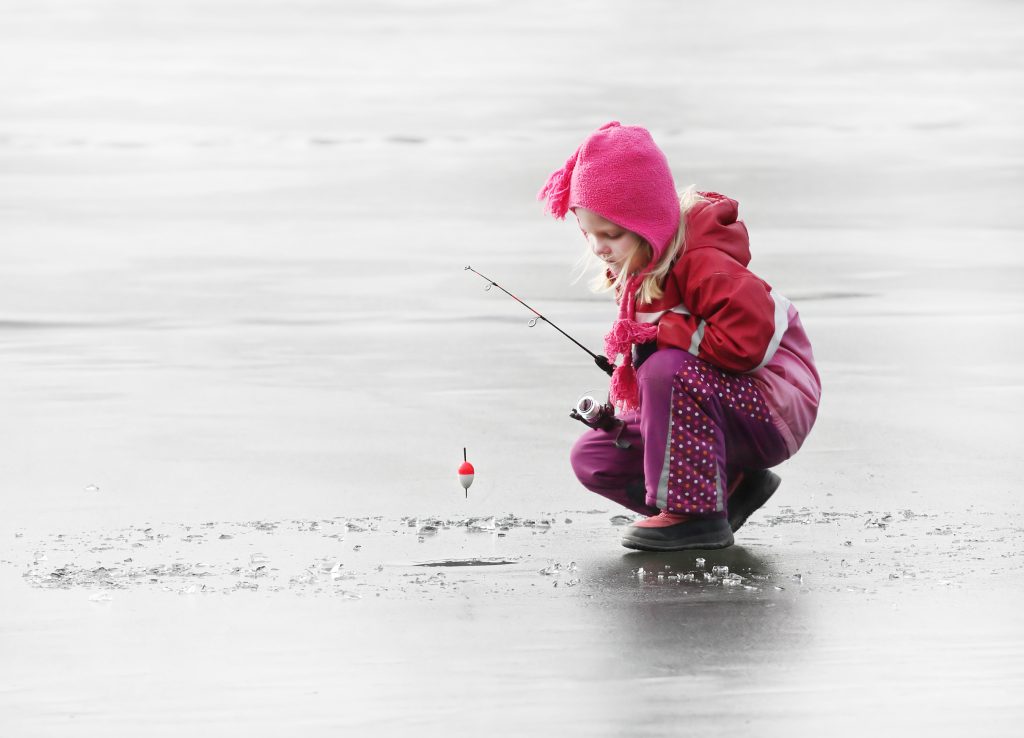A little girl standing on a frozen lake with an ice fishing rod