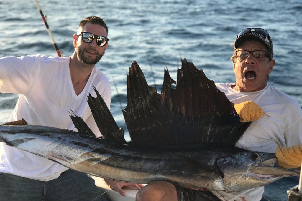 Dos hombres que sostienen un pez vela grande en un barco de alquiler