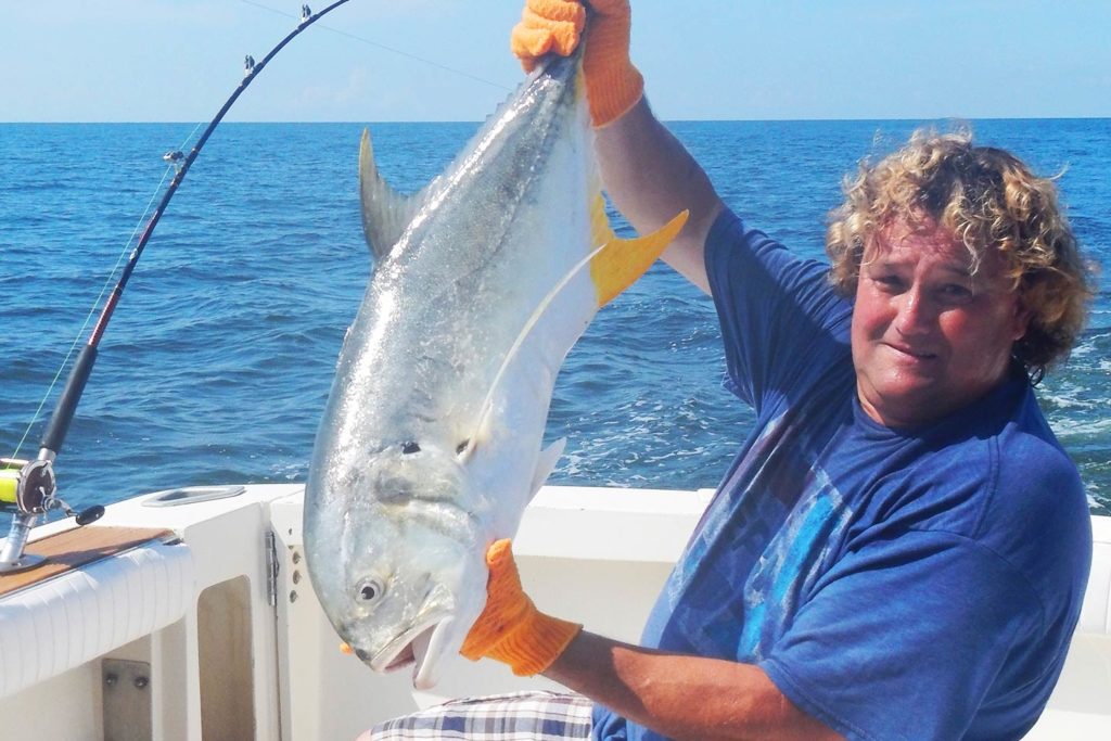 A male angler aboard a charter boat, holding a Jack Crevalle