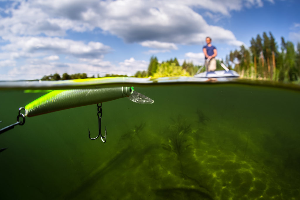 Split shot of the man fishing from the boat on the lake, with an underwater view of a jerkbait in the water.