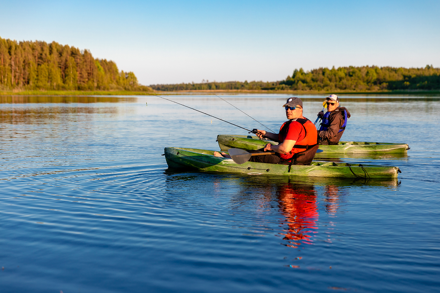 Two men kayak fishing together on a lake as part of a fishing therapy session