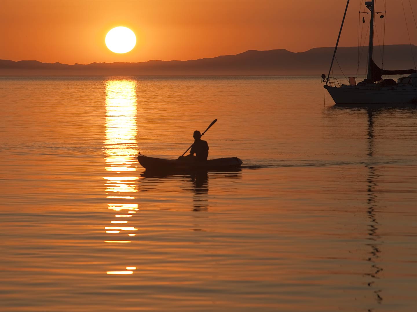 A kayaker paddles along the calm inshore waters out of La Paz as the sun sets.