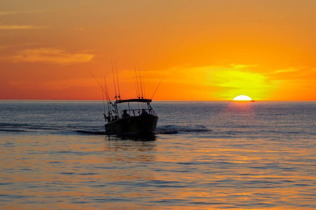 A boat trolls at sunset, with trolling lines visible.