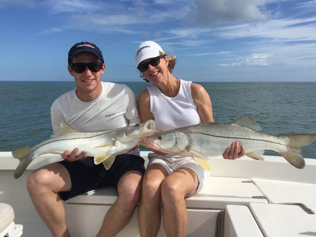 Een man en een vrouw houden elk een Snook vast aan boord van een platbodemboot, met het water op de achtergrond