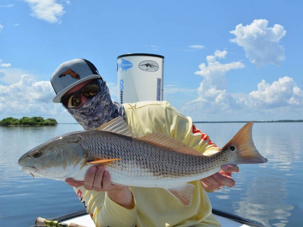 A man poses on a flats boat holding a big Redfish on the Indian River