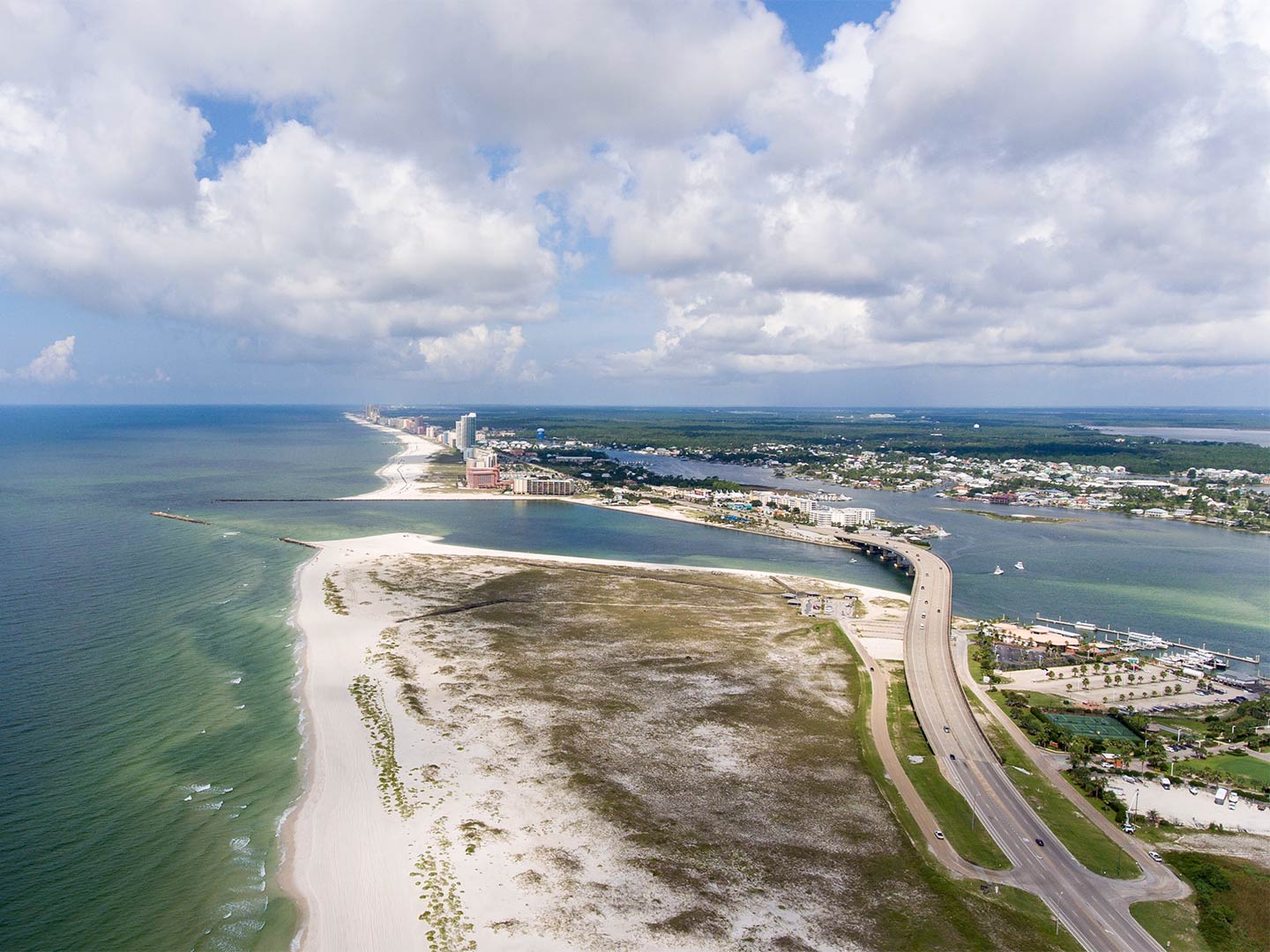 An aerial view of Orange Beach with the Gulf of Mexico on the left, a beach in the foreground, and a bridge on the right of the image