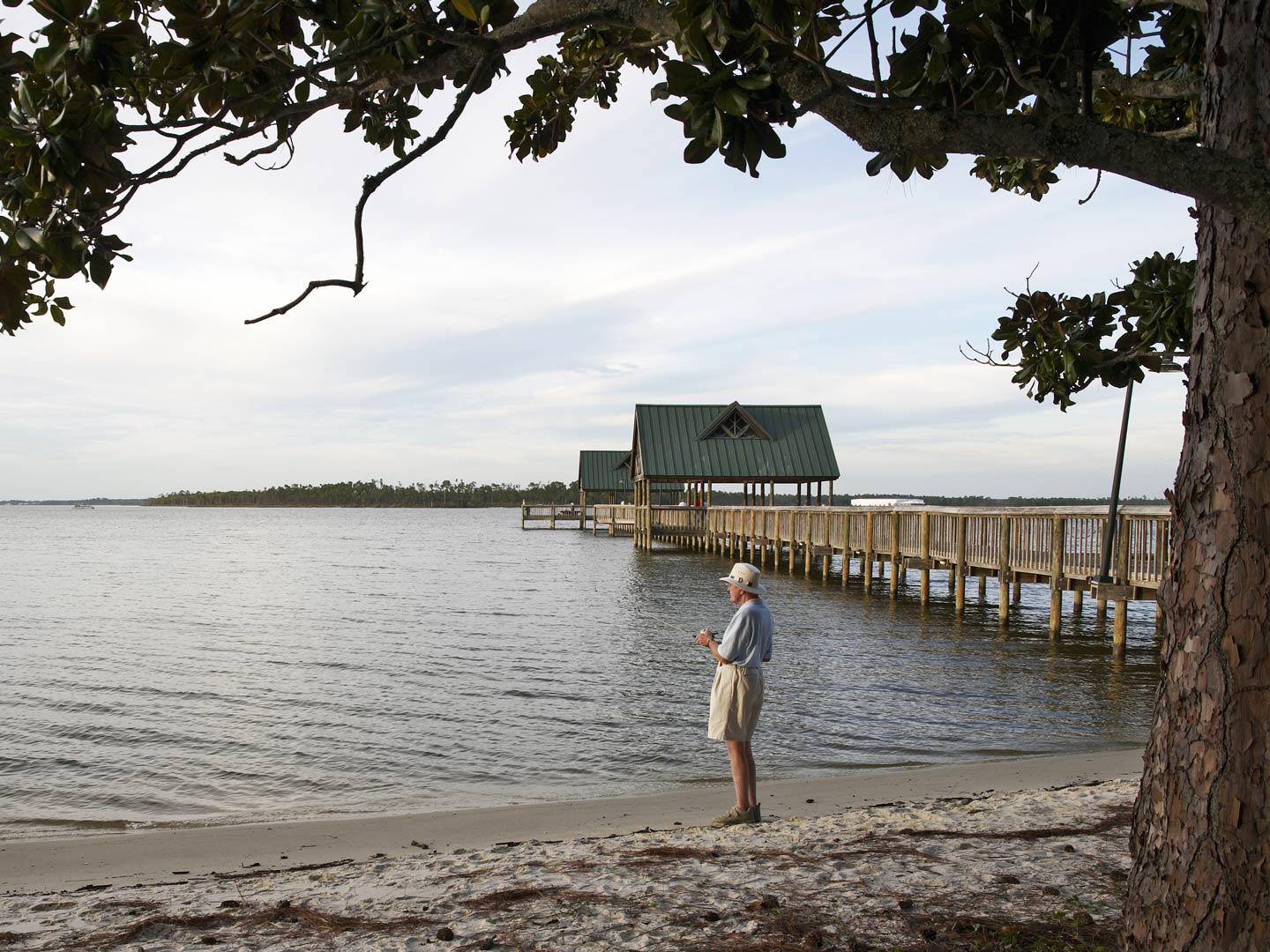 An elderly angler casts his line from shore next to a pier in Orange Beach.