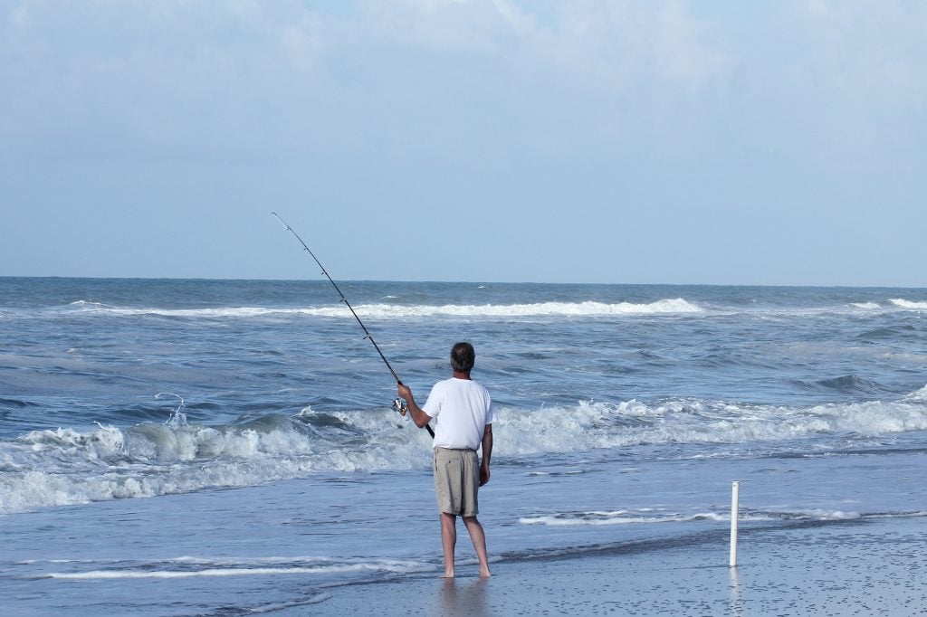 A man holding a fishing rod and surf fishing on the Outer Banks beach