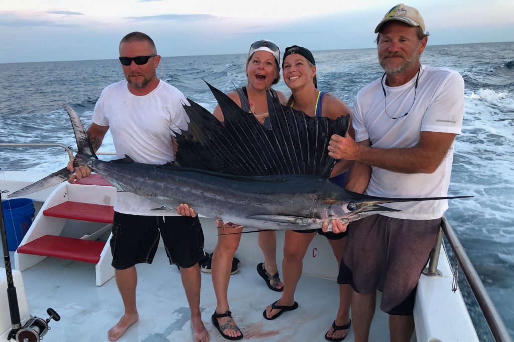 Two anglers posing with a large Sailfish caught out of Destin, with two crew members helping them hold the fish