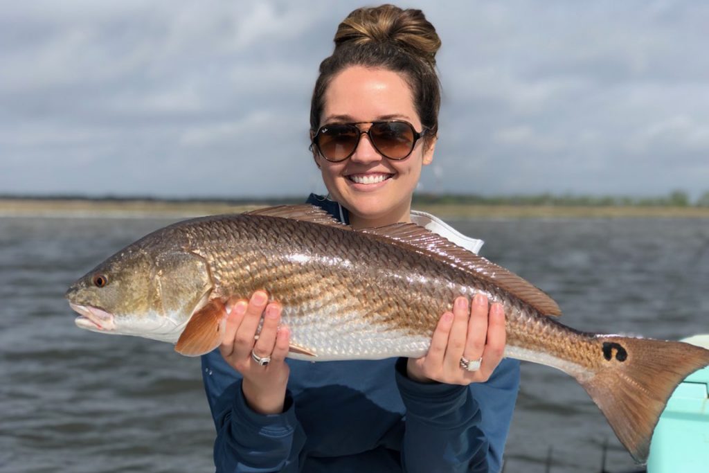 A happy woman holding a large Redfish caught while fishing in Pensacola