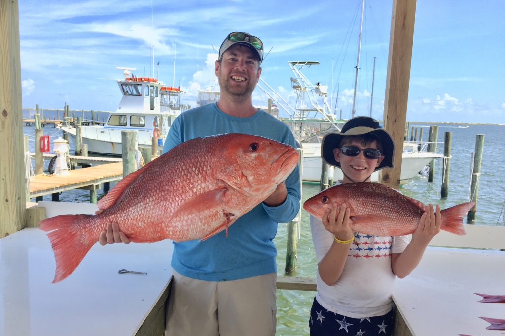 A man and a boy holding red and vermilion snapper caught on a fishing trip out of Pensacola, FL