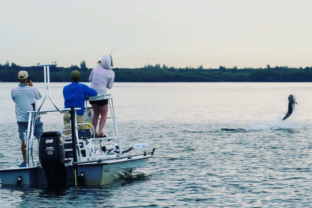 A woman fighting a Tarpon on a fishing charter in Pensacola, with two other anglers on the boat watching