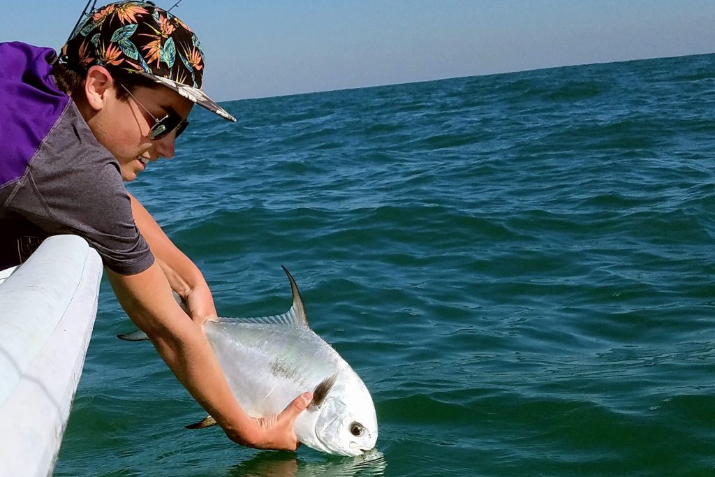 Un niño liberando un pez Permit de nuevo en el agua después de atraparlo