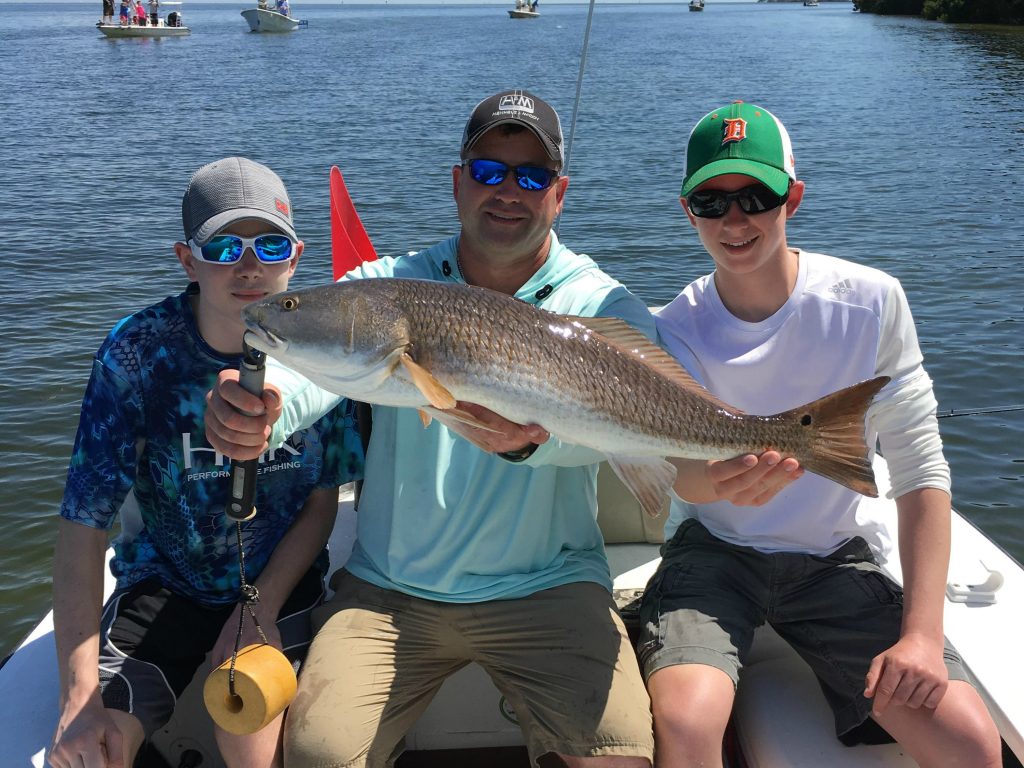 A father and two children sitting on a boat, holding a Redfish