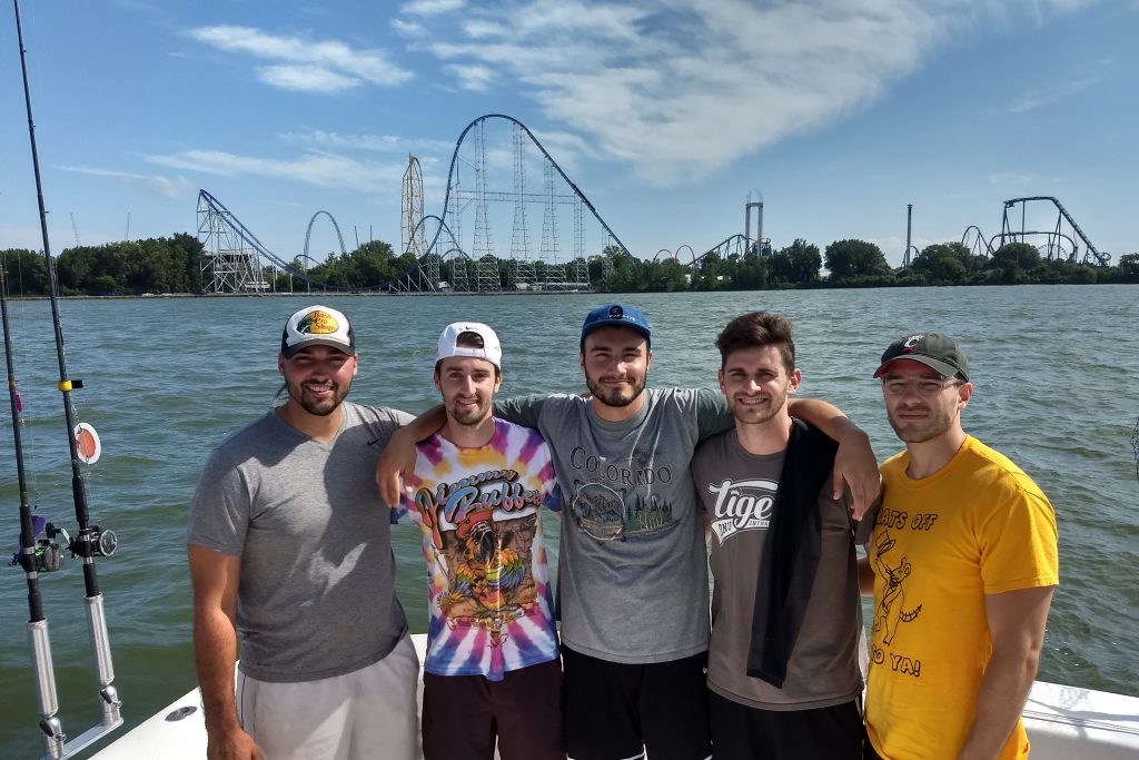A group of anglers on a charter fishing boat, with the rollercoasters of Sandusky in the distance behind them