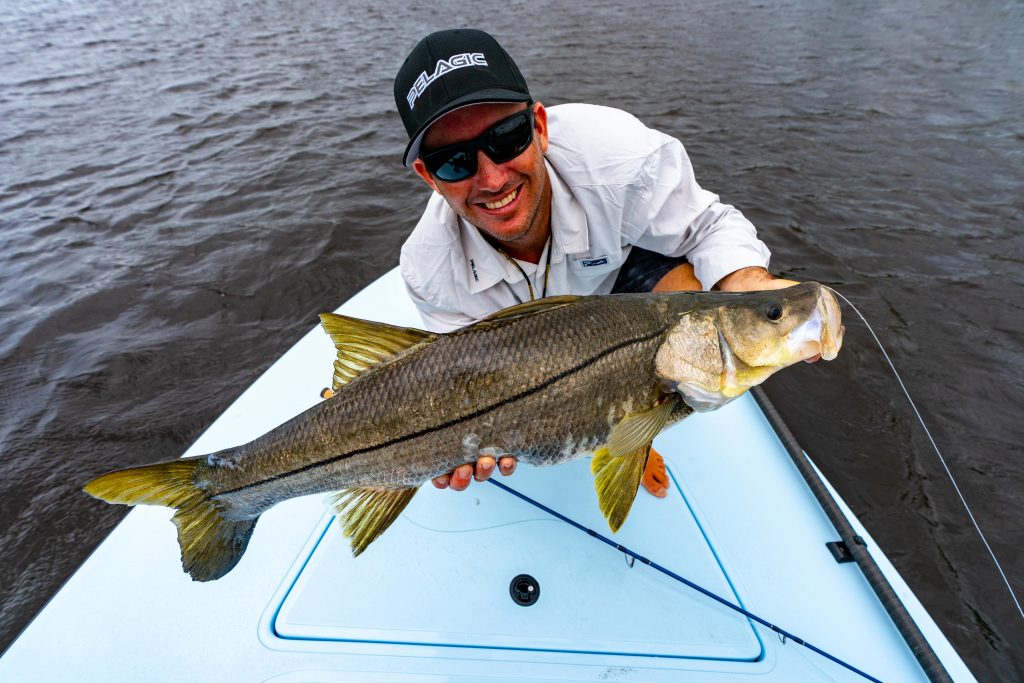 Een visser hurkt voorin een boot met een grote Snook