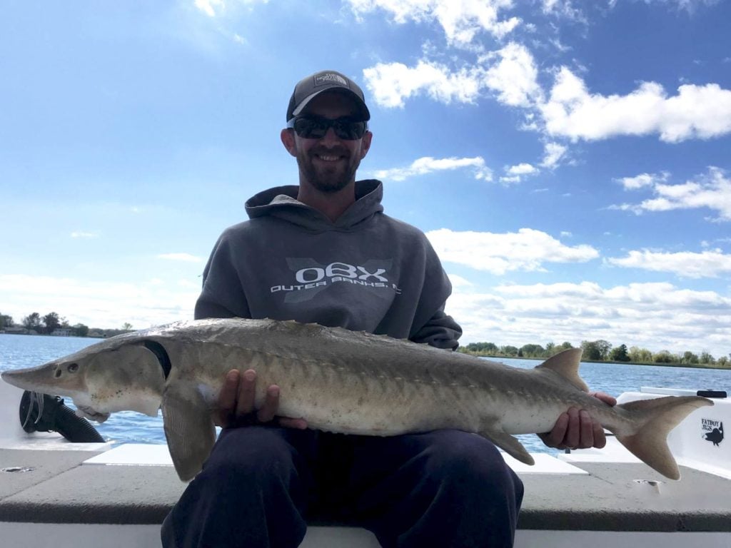 An angler holding a Sturgeon on a boat on Lake St. Clair