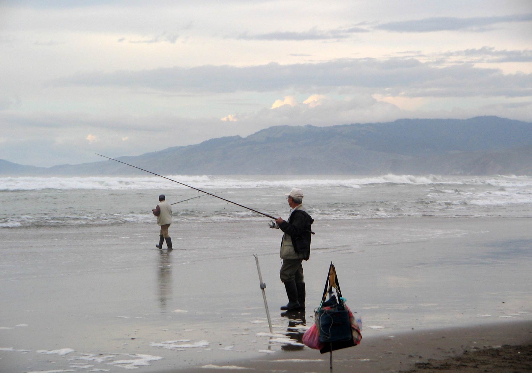 Two anglers fishing on a beach on a cloudy day
