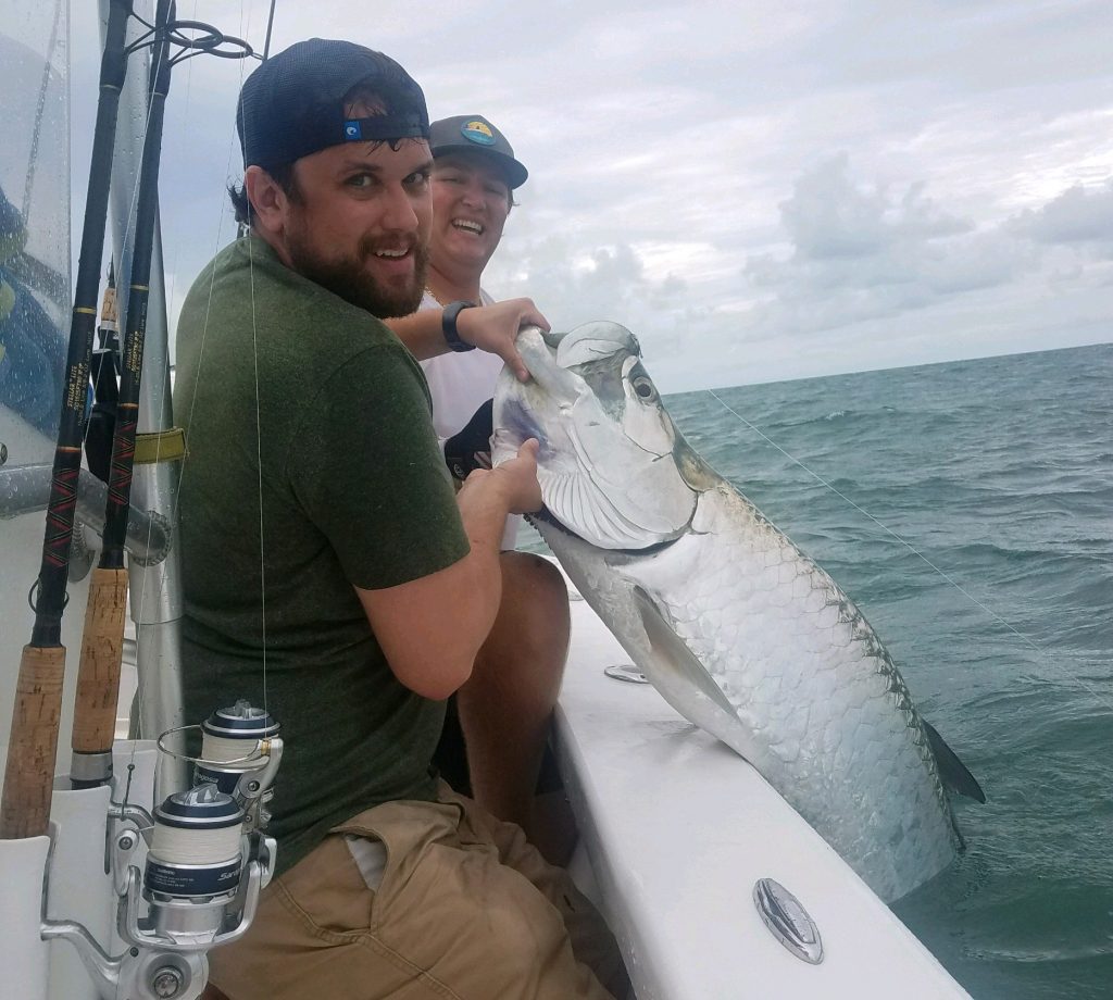 Two anglers holding a massive Tarpon halfway out of the water