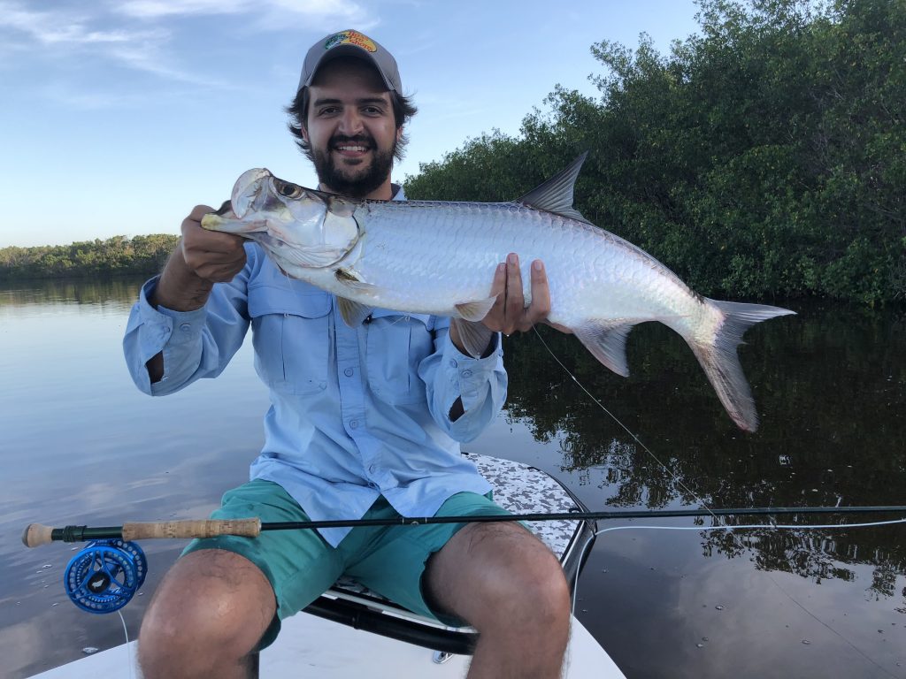 A Tarpon being held by a fisherman on a boat, caught while fly fishing in the Everglades