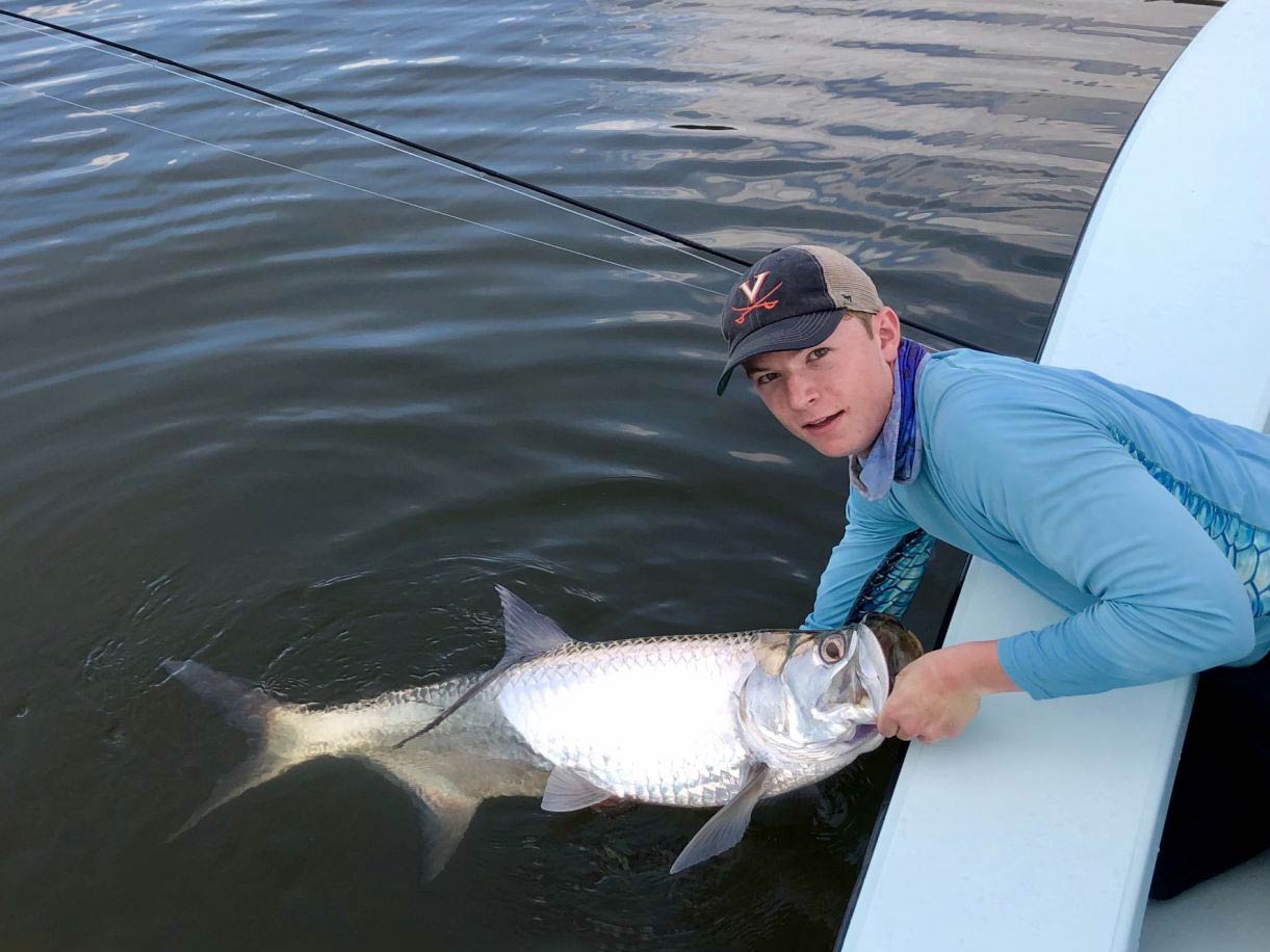 Een visser poseert met een Tarpon die hij net heeft gevangen terwijl hij de vis in het water houdt
