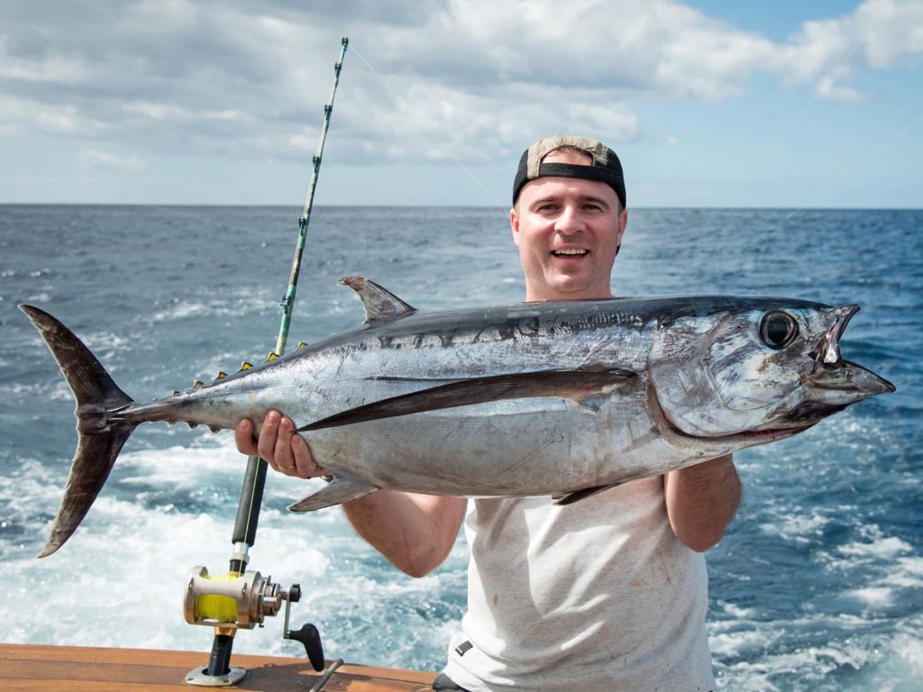A smiling angler, standing on a boat and holding a big Tuna