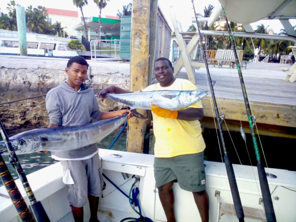 Two young fishermen standing on a fishing boat, holding two big Wahoo