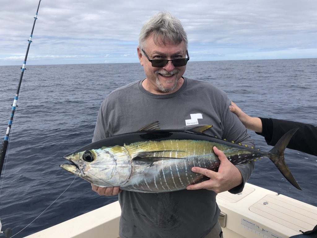 a smiling angler holding a Yellowfin Tuna on a fishing boat