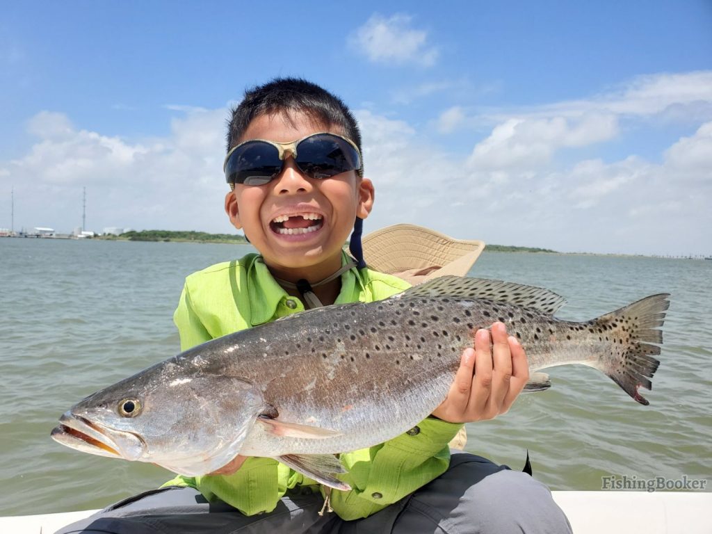 a young smiling angler holding a Spotted Seatrout he caught fishing the Texas coast